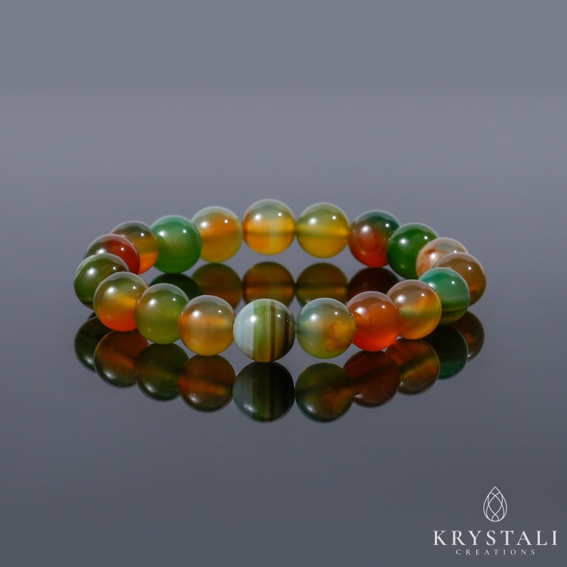 K&ouml;nnte beinhalten: Ein mehrfarbiges Agat-Armband mit gr&uuml;nen, orangefarbenen und braunen Perlen. Das Armband besteht aus nat&uuml;rlichen Steinen und hat eine polierte Oberfl&auml;che.