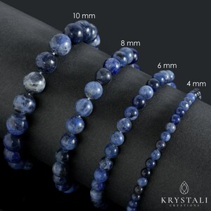 Op de afbeelding: Vier strengen blauwe edelsteen kralen, elk met een andere maat: 10 mm, 8 mm, 6 mm en 4 mm. De kralen zijn in een rij op een zwart oppervlak gerangschikt.