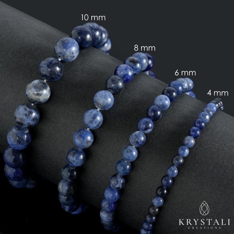 Op de afbeelding: Vier strengen blauwe edelsteen kralen, elk met een andere maat: 10 mm, 8 mm, 6 mm en 4 mm. De kralen zijn in een rij op een zwart oppervlak gerangschikt.