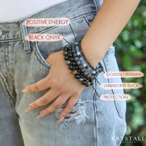 K&ouml;nnte beinhalten: Ein Stapel aus f&uuml;nf Armb&auml;ndern aus schwarzem Onyx, Labradorit, goldenem Obsidian und blauen Steinen. Die Armb&auml;nder sind mit ihren entsprechenden Bedeutungen beschriftet: "Positive Energie", "Schwarzer Onyx", "Schutz", "Labradorit Schwarz" und "Goldener Obsidian".