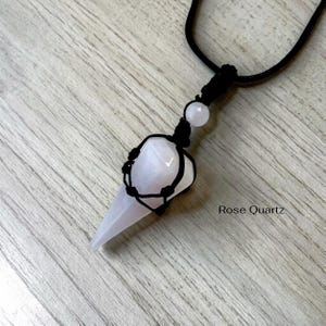 May include: A rose quartz pendulum necklace with a black cord. The light pink crystal is encased in a black woven net. The text "Rose Quartz" is at the bottom right.