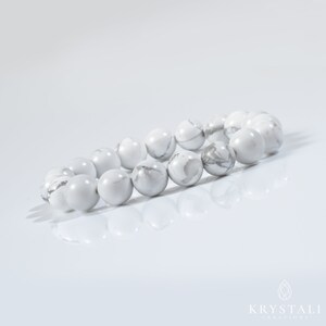 May include: White Howlite beaded bracelet with round beads. The bracelet is laid out on a white surface.
