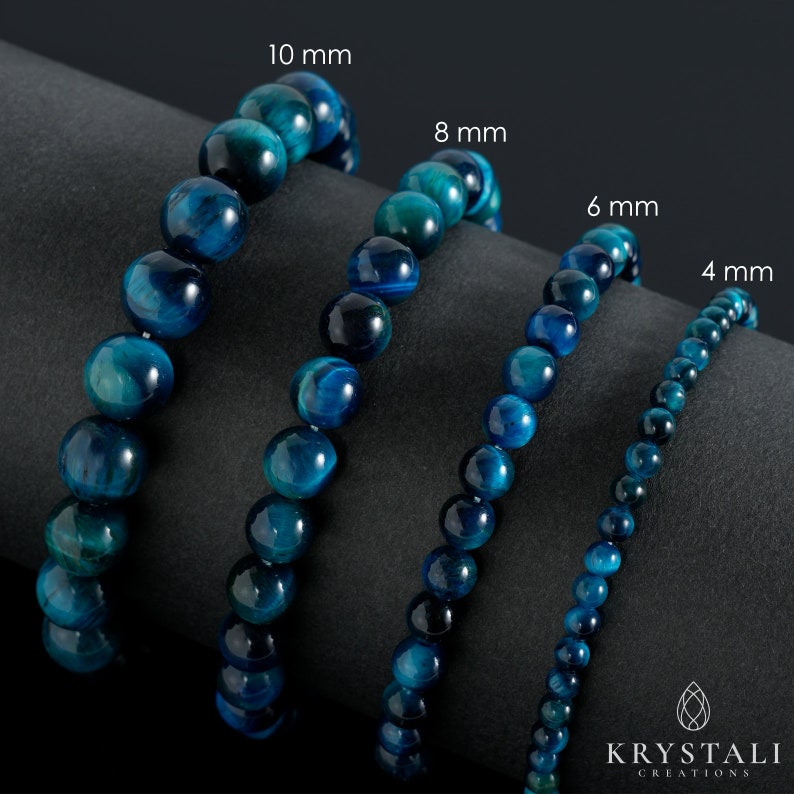 May include: Four blue tiger's eye gemstone bracelets of different sizes, 4 mm, 6 mm, 8 mm, and 10 mm, laid out on a black surface.