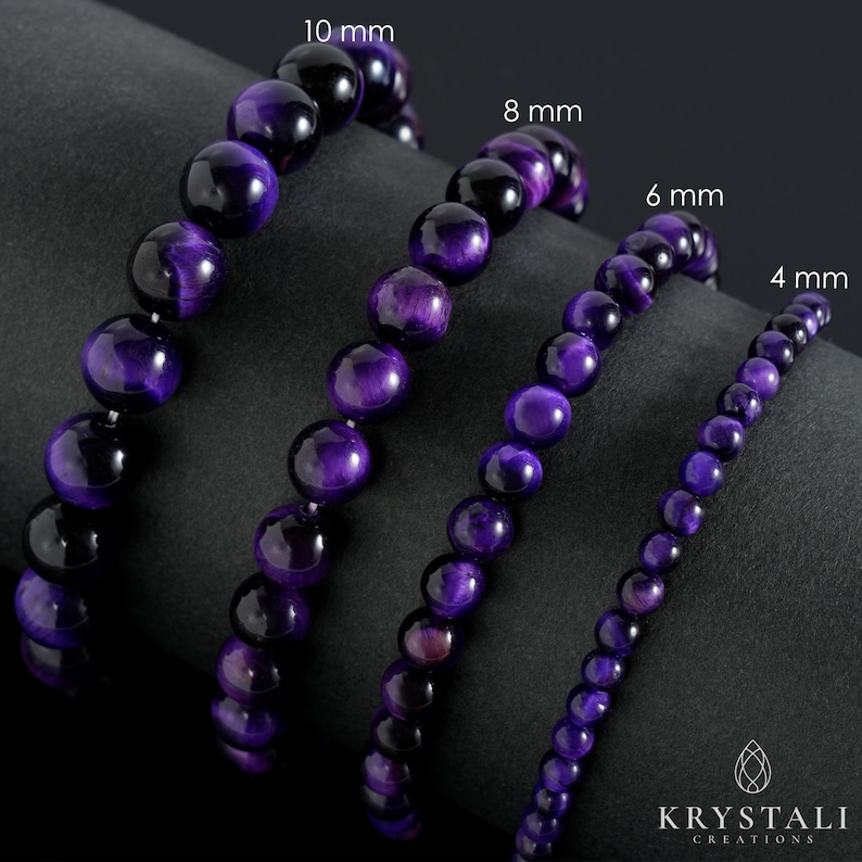 May include: Four purple tiger eye bead bracelets, with bead sizes of 4 mm, 6 mm, 8 mm, and 10 mm. The bracelets are displayed on a dark gray surface. The KRYSTALI CREATIONS logo is in the bottom right corner.