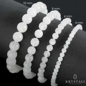 May include: Four white gemstone bracelets of different sizes, 4 mm, 6 mm, 8 mm, and 10 mm, laid out on a grey surface. The bracelets are made of round, smooth beads.