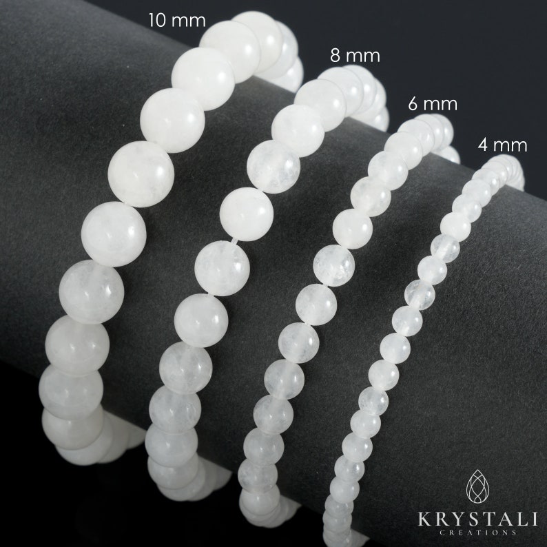 May include: Four white gemstone bracelets of different sizes, 4 mm, 6 mm, 8 mm, and 10 mm, laid out on a grey surface. The bracelets are made of round, smooth beads.