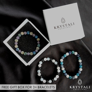K&ouml;nnte beinhalten: Drei Edelstein-Armb&auml;nder in einer wei&szlig;en Box. Die Armb&auml;nder bestehen aus blauen, gr&uuml;nen und wei&szlig;en Steinen. Die Box tr&auml;gt den Text "Krystali Creations". Kostenlose Geschenkbox f&uuml;r 3+ Armb&auml;nder.