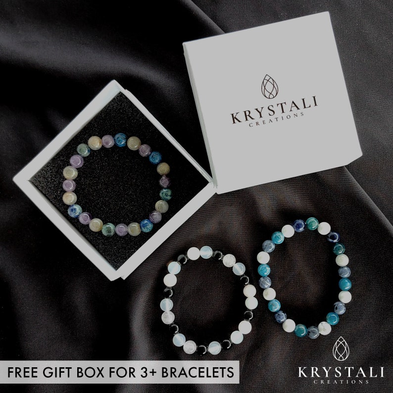 K&ouml;nnte beinhalten: Drei Edelstein-Armb&auml;nder in einer wei&szlig;en Box. Die Armb&auml;nder bestehen aus blauen, gr&uuml;nen und wei&szlig;en Steinen. Die Box tr&auml;gt den Text "Krystali Creations". Kostenlose Geschenkbox f&uuml;r 3+ Armb&auml;nder.