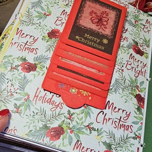 Może przedstawiać: Stos czerwono-brązowych kartek świątecznych z zielono-białym wzorem kwiatowym. Na kartkach widnieje napis "Merry Christmas" i "Holidays".