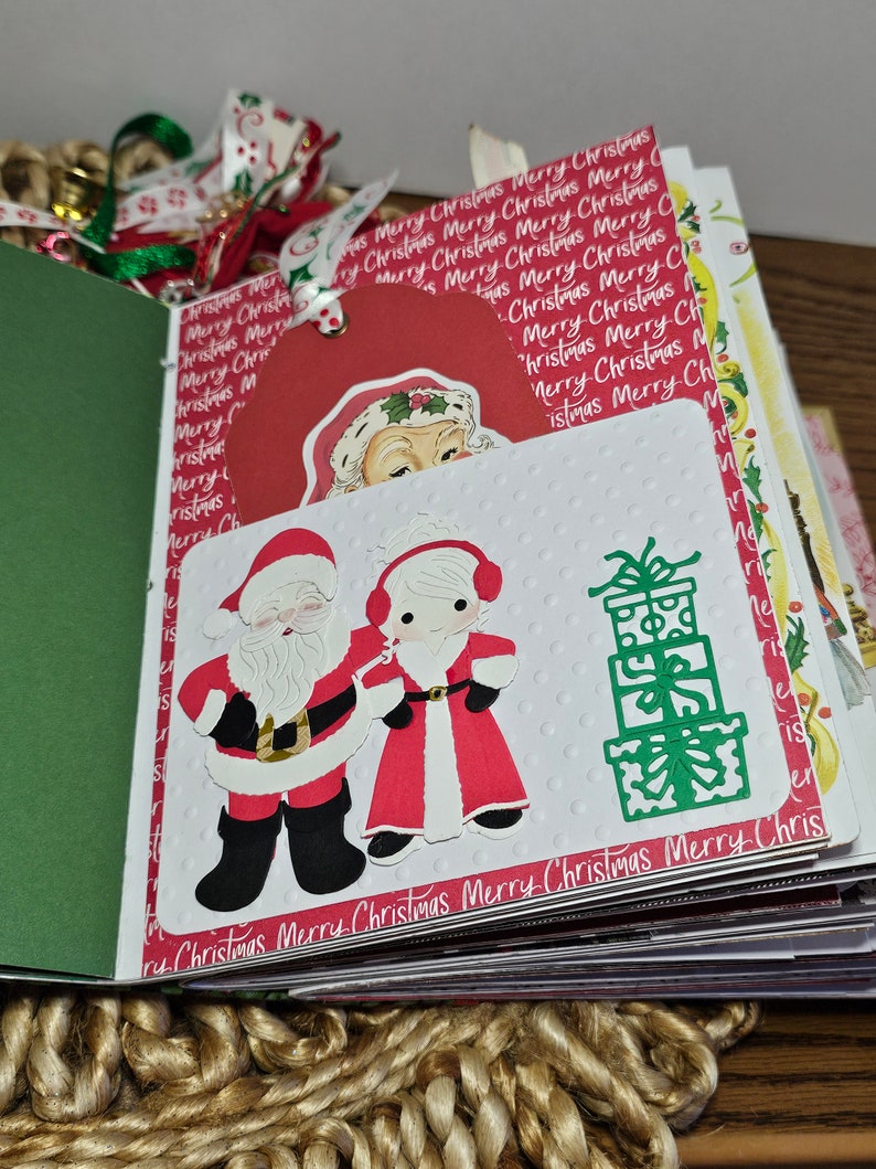Może przedstawiać: Album scrapbookingu o tematyce świątecznej z białą stroną przedstawiającą Świętego Mikołaja i Panią Mikołajową w czerwieni i bieli, zielony stos prezent&oacute;w oraz tekst "Merry Christmas Merry Christmas Merry Christmas Merry Chris".