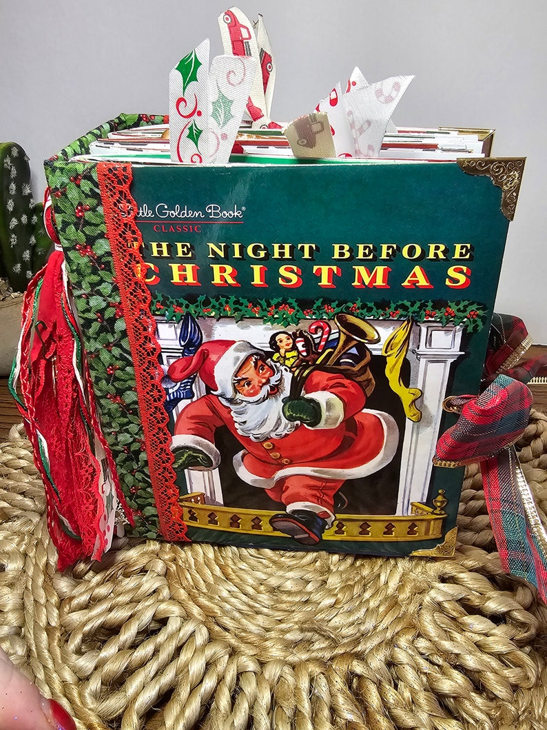 Może przedstawiać: Antyczna książka Little Golden Book zatytułowana "Noc przed Bożym Narodzeniem" z zieloną okładką i obrazkiem Świętego Mikołaja niosącego worek z zabawkami. Książka jest ozdobiona czerwoną i zieloną wstążką, koronką i resztkami tkaniny.