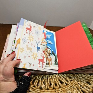 May include: A Christmas themed scrapbook with a red cover and pages decorated with reindeer and snowflakes. The scrapbook is open to reveal a page with a vintage Christmas card featuring Santa Claus and reindeer.