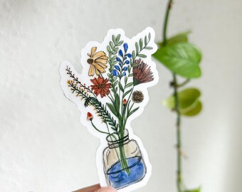 Può includere: Un adesivo con un bouquet di fiori selvatici disegnato a mano in un barattolo di vetro blu. I fiori sono gialli, arancioni, rossi, blu e verdi.