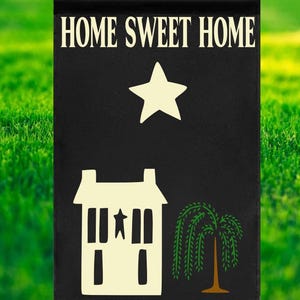 May include: Black garden flag with the words "HOME SWEET HOME" in white. A white star, a house, and a weeping willow tree are also featured. The flag is displayed against a backdrop of green grass.
