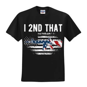 May include: Black t-shirt with the text "I 2ND THAT" in white block letters. Below the text is a graphic of a rifle in red, white, and blue, superimposed over a distressed American flag design.