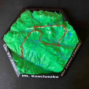 Könnte beinhalten: Grüne 3D-Topografische Karte des Mt. Kosciuszko, mit einem roten Wanderweg markiert. Die Karte befindet sich in einem schwarzen sechseckigen Rahmen, mit Text, der eine 37,25 km lange Wanderung in 8 Stunden 25 Minuten über 2 Tage angibt.