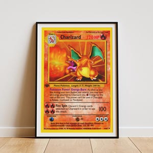 May include: A framed print of a Charizard trading card featuring the orange dragon-like creature breathing fire. The card displays 120 HP, the Energy Burn power, and the Fire Spin attack. The text includes details about the Flame Pokemon.
