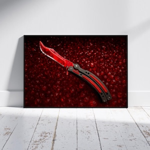 May include: A framed print featuring a butterfly knife with a blood-red blade and accents. The knife is set against a textured, dark red background. The handle has black and red details.
