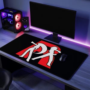 Puede incluir: Alfombrilla de ratón para juegos rectangular negra con un diseño gráfico rojo y blanco. El diseño presenta dos figuras estilizadas y la letra "R". Un ratón de ordenador negro está en el lado derecho de la alfombrilla.