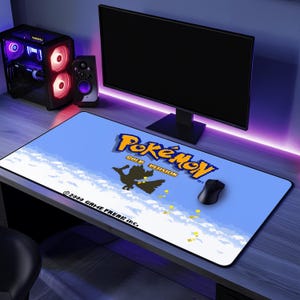 May include: A blue and white gaming mouse mat with a pixelated image of a bird flying in the sky. The text "Pokémon Gold Version" is printed in yellow and orange. The copyright text "© 2000 GAME FREAK inc." is printed in white.