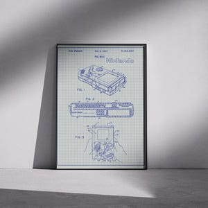 以下が含まれることがあります： 任天堂の携帯型ゲーム機の青写真スタイルのフレーム入りプリント。プリントには、複数のビューや内部コンポーネントを含む、デバイスの詳細な技術図面が掲載されており、上部には任天堂のロゴがあります。プリントは黒いフレームに入っています。