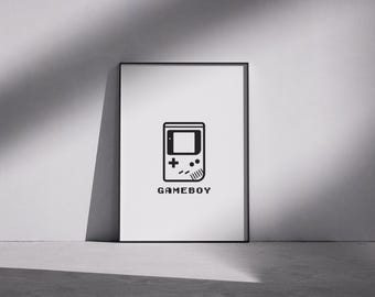 Può includere: Una stampa incorniciata con un'illustrazione in bianco e nero di Gameboy. Il design presenta il contorno della console Gameboy con la scritta "GAMEBOY" sotto. La stampa è esposta su uno sfondo grigio neutro.