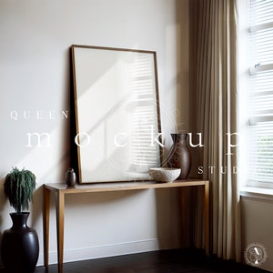 May include: A gold framed mirror hangs above a wooden console table with a brown vase and a white bowl. The table is in front of a white wall and a beige curtain. The window behind the curtain has white blinds.