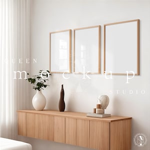 Puede incluir: Tres marcos de fotos vacíos con marcos de madera natural cuelgan de una pared blanca sobre un armario de madera clara. El armario tiene cuatro puertas y está decorado con un jarrón de plantas verdes, un jarrón marrón y un globo terráqueo decorativo.