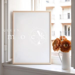 May include: A light wood frame with a white mat and a white background sits on a windowsill.  A vase with orange flowers sits on the windowsill to the right of the frame.