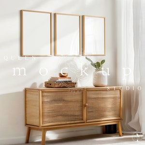 May include: Three gold framed square mirrors hang on a white wall above a light brown wooden cabinet with a woven rattan front. A small potted plant sits on the cabinet.