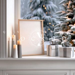 May include: A wooden picture frame with a white mat and a blank white canvas. The frame is sitting on a white windowsill with two candles and two wrapped gifts in front of it. The windowsill is in front of a window with a snowy winter scene outside.