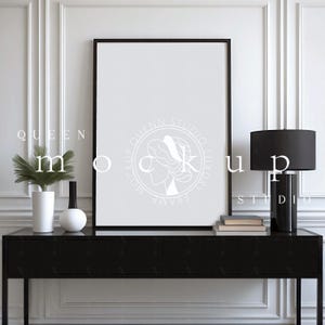 Puede incluir: Una maqueta de impresión enmarcada en negro sobre una consola negra. La mesa tiene un jarrón blanco con una planta, un jarrón negro y una esfera blanca. Una lámpara negra y libros están a la derecha. La pared es blanca con molduras. El texto "QUEEN MOCKUP STUDIO LUXURY FRAME".