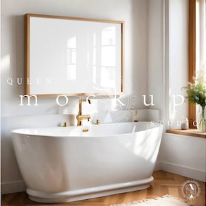 May include: A white bathtub with gold faucets in a bathroom with a large framed mirror and a window with white flowers in a vase.