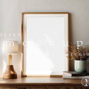 Può includere: Un tavolo di legno con un quadro incorniciato, una lampada e un vaso con fiori secchi. La cornice del quadro è marrone chiaro con un passepartout bianco e uno sfondo bianco. La lampada è in legno e ha un paralume bianco. Il vaso è blu chiaro e i fiori sono beige. Il tavolo è in legno e ha una finitura marrone chiaro.