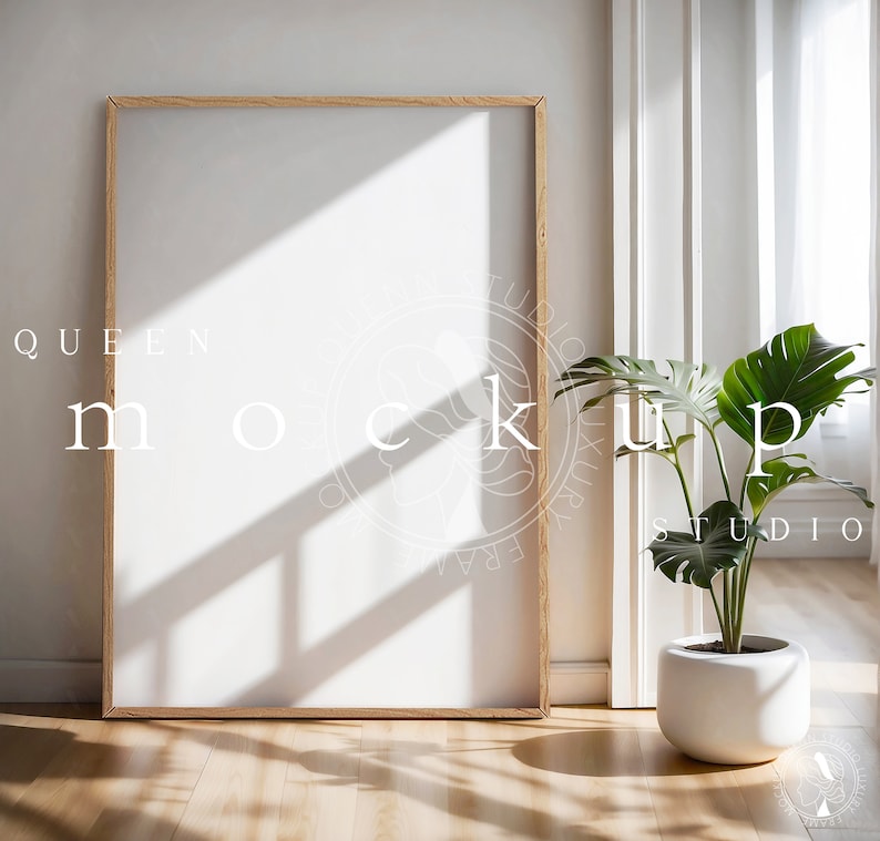 May include: A large, light wood framed poster mockup with a white background. The poster is leaning against a white wall. A potted plant with large green leaves is in the foreground. The plant is in a white ceramic pot.