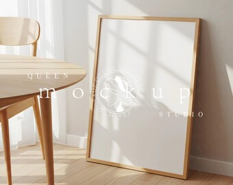 Può includere: Una cornice rettangolare in legno è appoggiata a un muro. Un tavolo e una sedia in legno sono in primo piano. Il poster ha uno sfondo bianco con un logo e testo. La scena è illuminata dalla luce naturale.