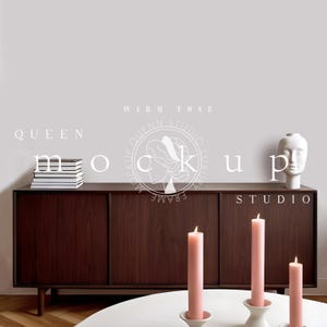 May include: A dark brown wooden cabinet with three drawers and three doors. The cabinet is standing on a light wood floor. There are three pink candles on a white table in front of the cabinet. The text "QUEEN STUDIO LUXURY FRAME" is visible on the cabinet.