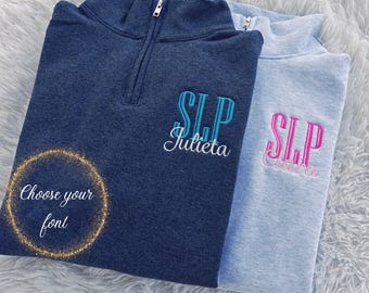 May include: Two quarter-zip pullovers, one navy blue and one light blue, embroidered with initials and names. The navy blue pullover has teal embroidery, while the light blue one has pink embroidery. The text "Choose your font" is also visible.