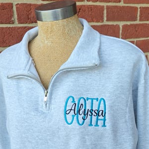 May include: Gray quarter-zip sweatshirt with a blue and black embroidered monogram that says "Alyssa".