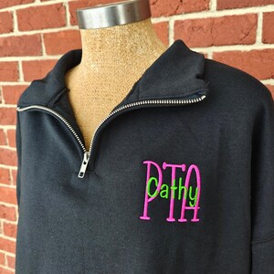 May include: Black quarter-zip sweatshirt with a pink and green embroidered monogram that says "PTA Cathy"