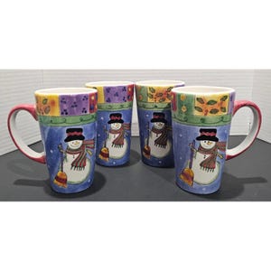 May include: A set of four tall ceramic mugs featuring a blue base with a white snowman wearing a black top hat and a red and green striped scarf. The snowman holds a broom. The top rim has a decorative border of purple, yellow, and green squares.