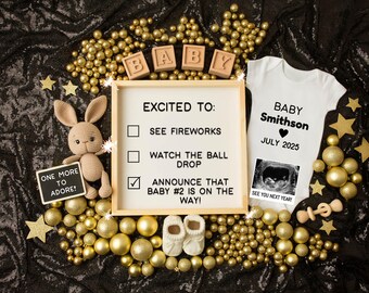 May include: A pregnancy announcement with gold and black decorations. A chalkboard sign reads "One More To Adore!" A wooden sign reads "Excited To: Announce That Baby #2 Is On The Way!" A white onesie reads "Baby Smithson July 2025" with a sonogram image.
