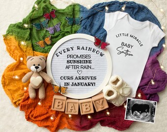 May include: A baby announcement featuring a white babygrow, ultrasound scan, and wooden blocks spelling "BABY." The announcement includes a letter board with text and a crocheted teddy bear. Decorative butterflies and a rainbow-coloured fabric complete the scene.