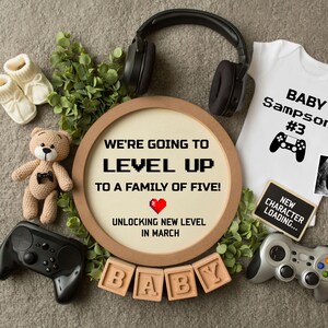 May include: A pregnancy announcement with a video game theme. A wooden sign reads "We're going to level up to a family of five! Unlocking new level in March."  A white onesie reads "Baby Sampson #3" with a video game controller graphic.  A small ultrasound image is included.