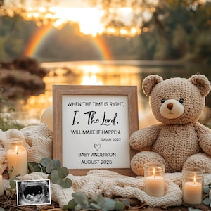 Puede incluir: Un cartel enmarcado con una cita religiosa sobre el Señor que hace que las cosas sucedan. El cartel está sentado sobre una manta blanca con un oso de peluche y velas. La cita es "Cuando el tiempo es correcto, yo, el Señor. Haré que suceda. Isaías 60:22". El cartel también dice "Baby Anderson Agosto 2025".
