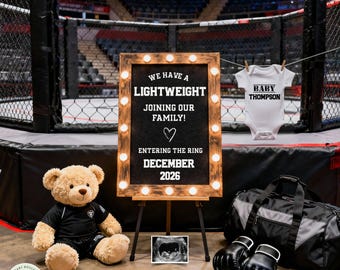 May include: An announcement for a baby with a boxing theme. A framed sign with the text "We have a lightweight joining our family! Entering the ring December 2026" is displayed. A teddy bear, baby clothes, boxing gloves, and a duffel bag are also present.