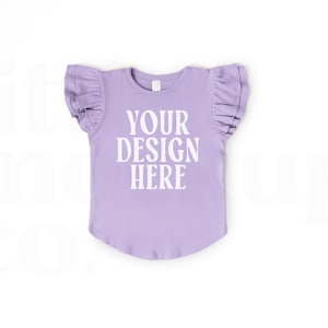 Puede incluir: Una camiseta de manga corta de color lavanda con mangas con volantes. La camiseta tiene el texto "YOUR DESIGN HERE" impreso en la parte delantera.