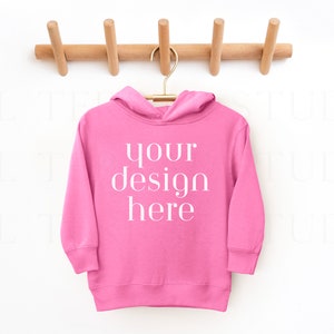 May include: Pink hooded sweatshirt hanging on a wooden rack with the text "your design here" printed on the front.
