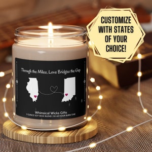 May include: A brown soy wax candle with a black label that reads "Through the Miles, Love Bridges the Gap". The label features a map of Illinois and Indiana with a heart in each state and a dotted line connecting them. The candle is on a wooden base and surrounded by string lights. The text "CUSTOMIZE WITH STATES OF YOUR CHOICE!" is in a yellow hexagon.