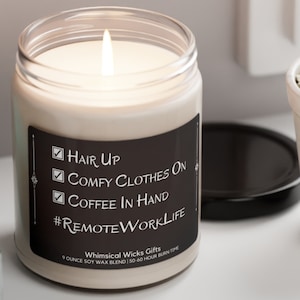May include: A white soy wax candle in a clear glass jar with a black label. The label has a checklist with the text "Hair Up", "Comfy Clothes On", and "Coffee In Hand". The label also includes the hashtag "#RemoteWorkLife". The candle is 9 ounces and has a 50-60 hour burn time.